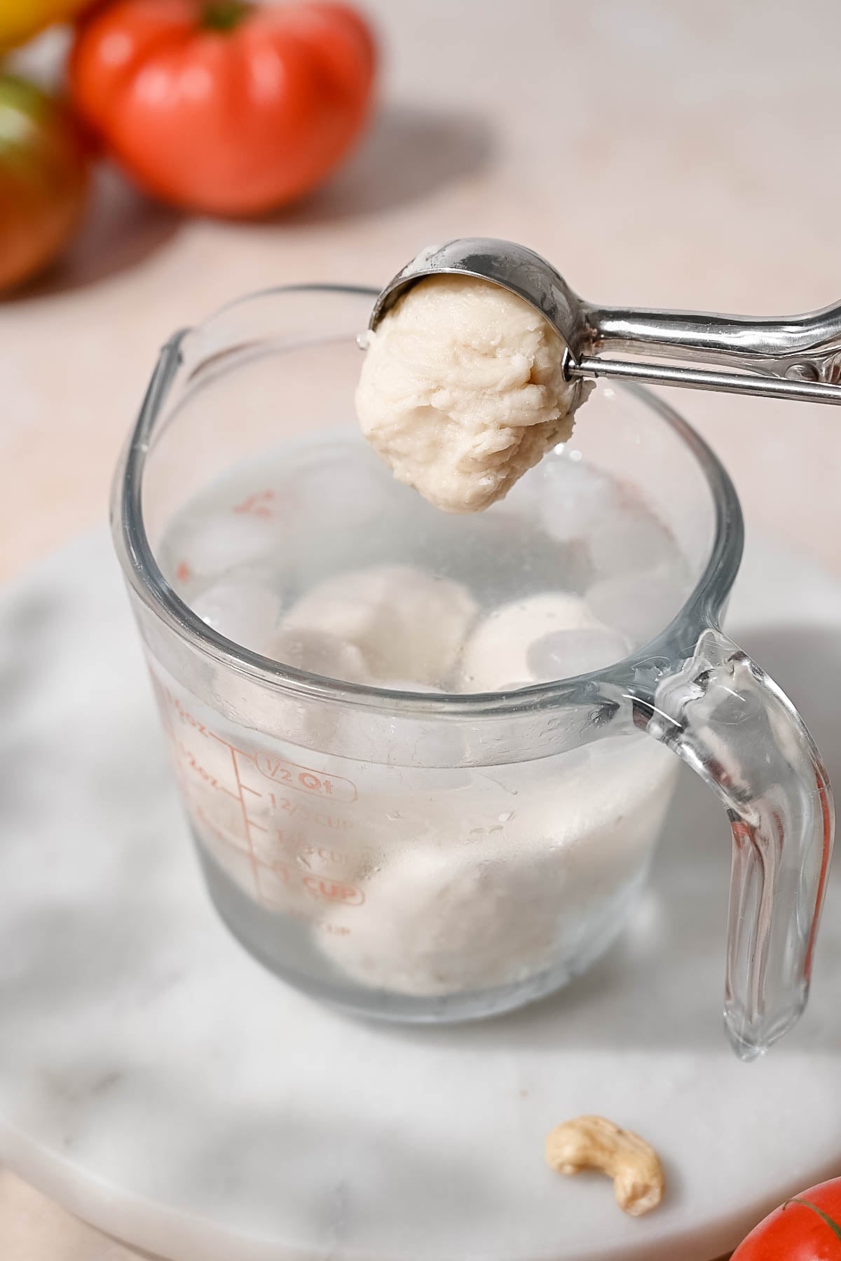 A scoop of homemade vegan mozzarella being shaped over ice water with several finished balls below.