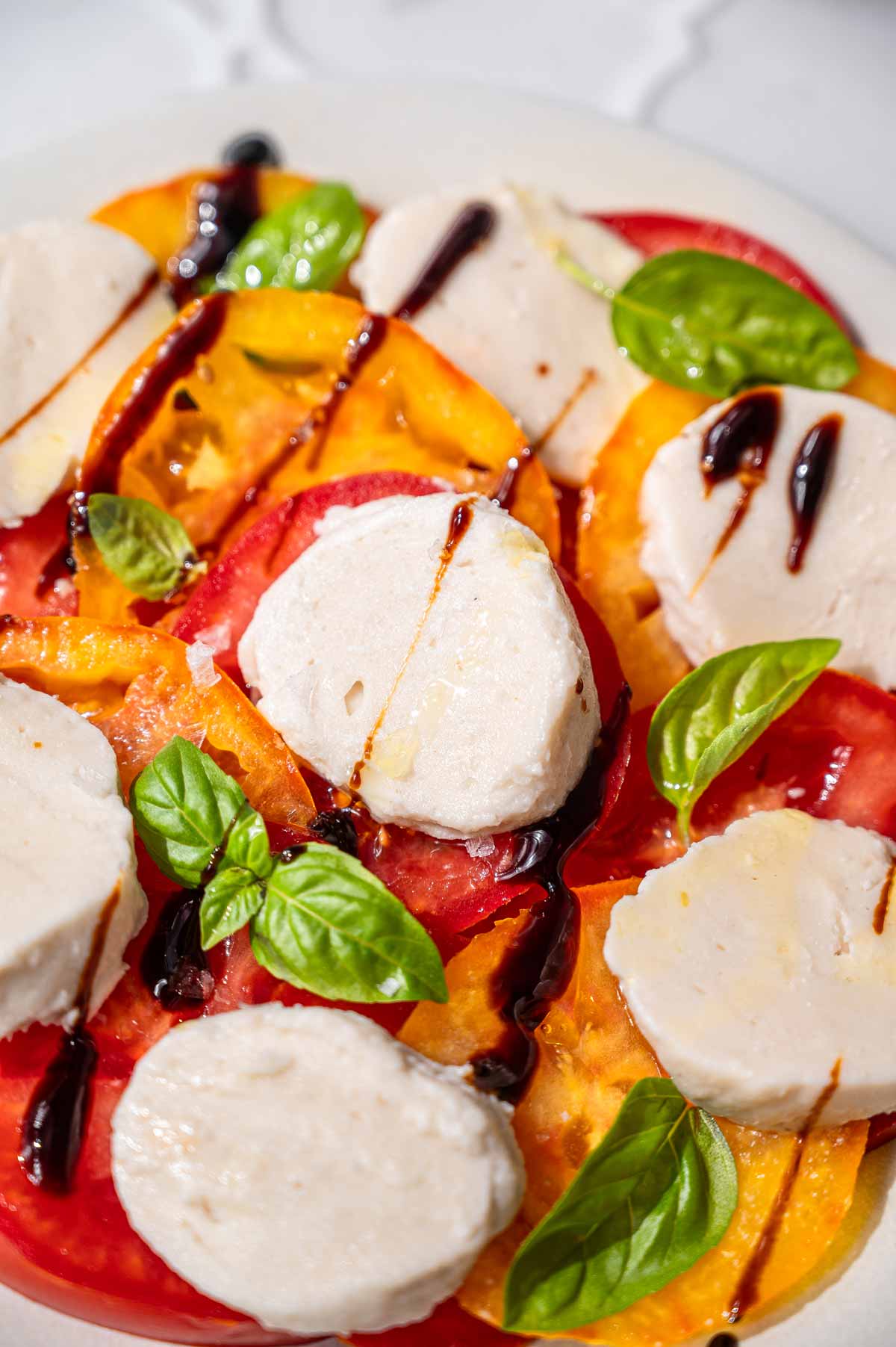 Close-up of vegan mozzarella slices with heirloom tomatoes, fresh basil, olive oil, and balsamic glaze.