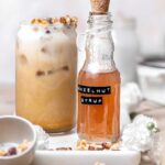 a jar of hazelnut simple syrup next to a hazelnut latte on a marble board.