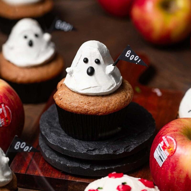 a cupcake with frosting in the shape of a ghost holding a flag that reads 'boo'.
