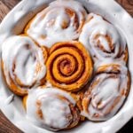 a baking tray with vegan pumpkin spice cinnamon rolls topped with cream cheese frosting.