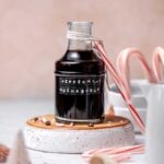 A jar filled with peppermint mocha simple syrup on an upside down white bowl.