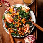warm kale salad with honeynut squash, maple dressing, apples and pomegranates on a plate.