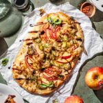 caramelized onion flatbread with sliced apples and balsamic glaze on crumpled parchment paper.