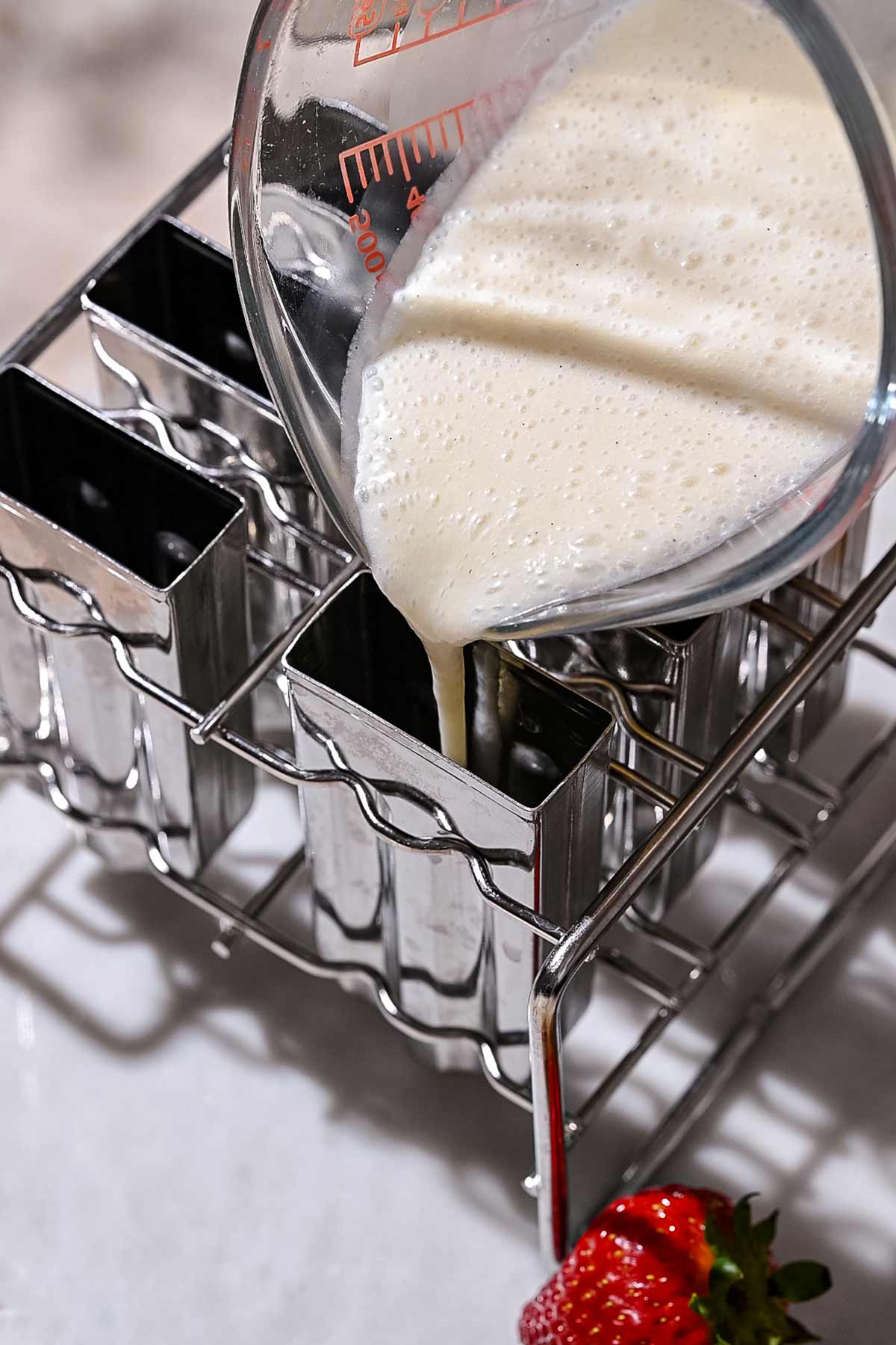 the dairy-free vanilla ice cream based being poured into a metal popsicle mold.