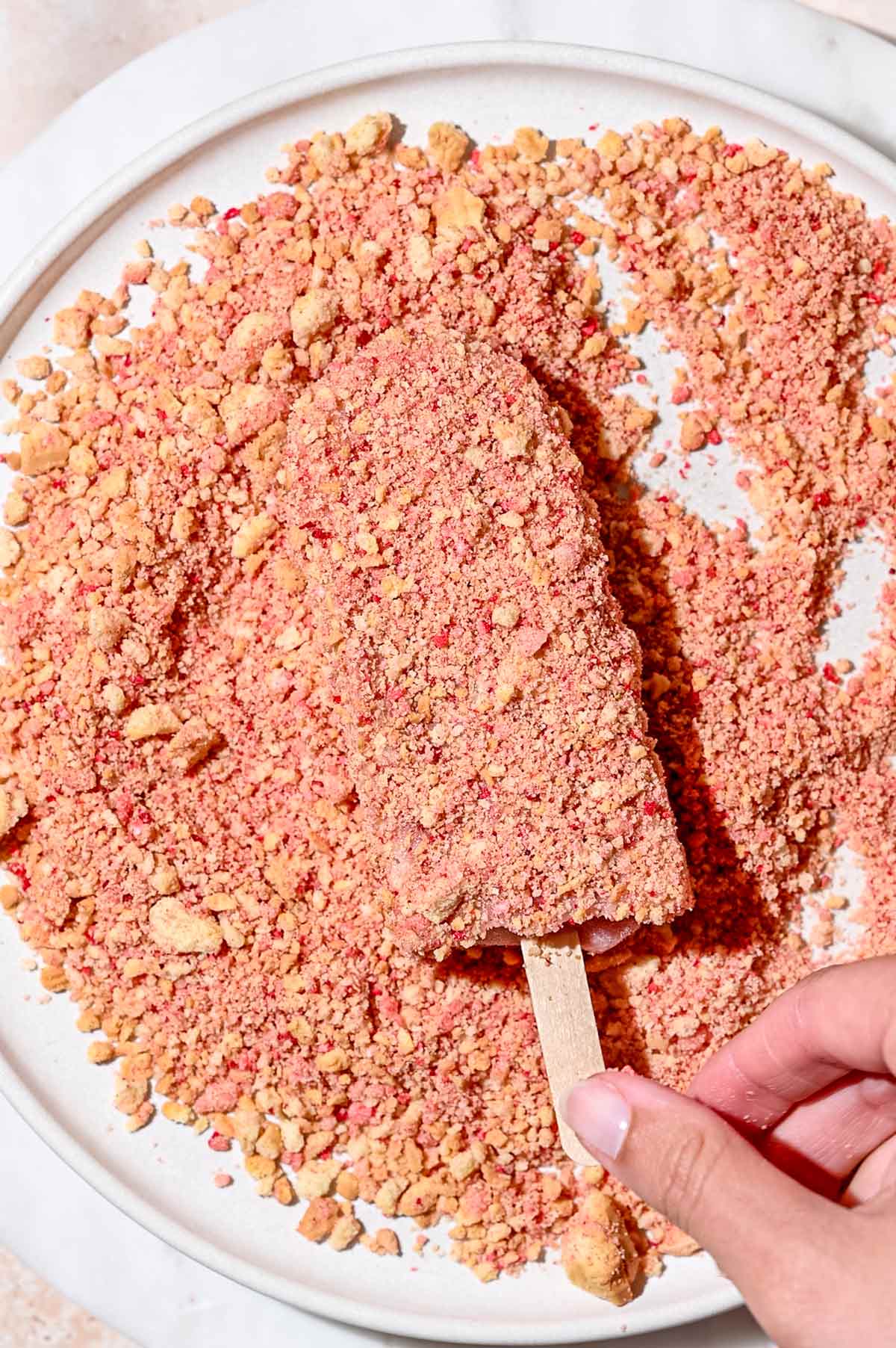 a hand putting an ice cream bar on shortcake crumbles.