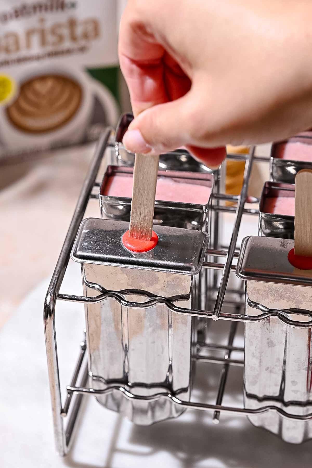 a hand placing a popsicle stick in the strawberry ice cream bars.