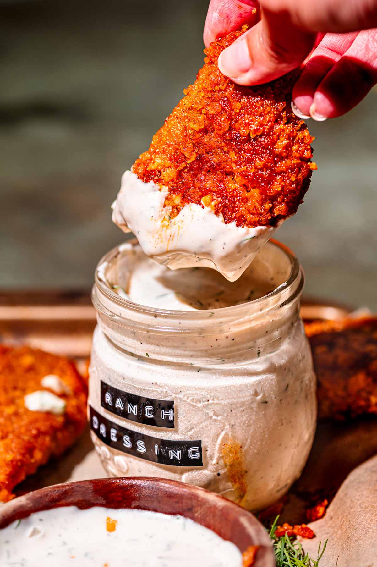 a hand dipping the vegan buffalo wings in ranch.