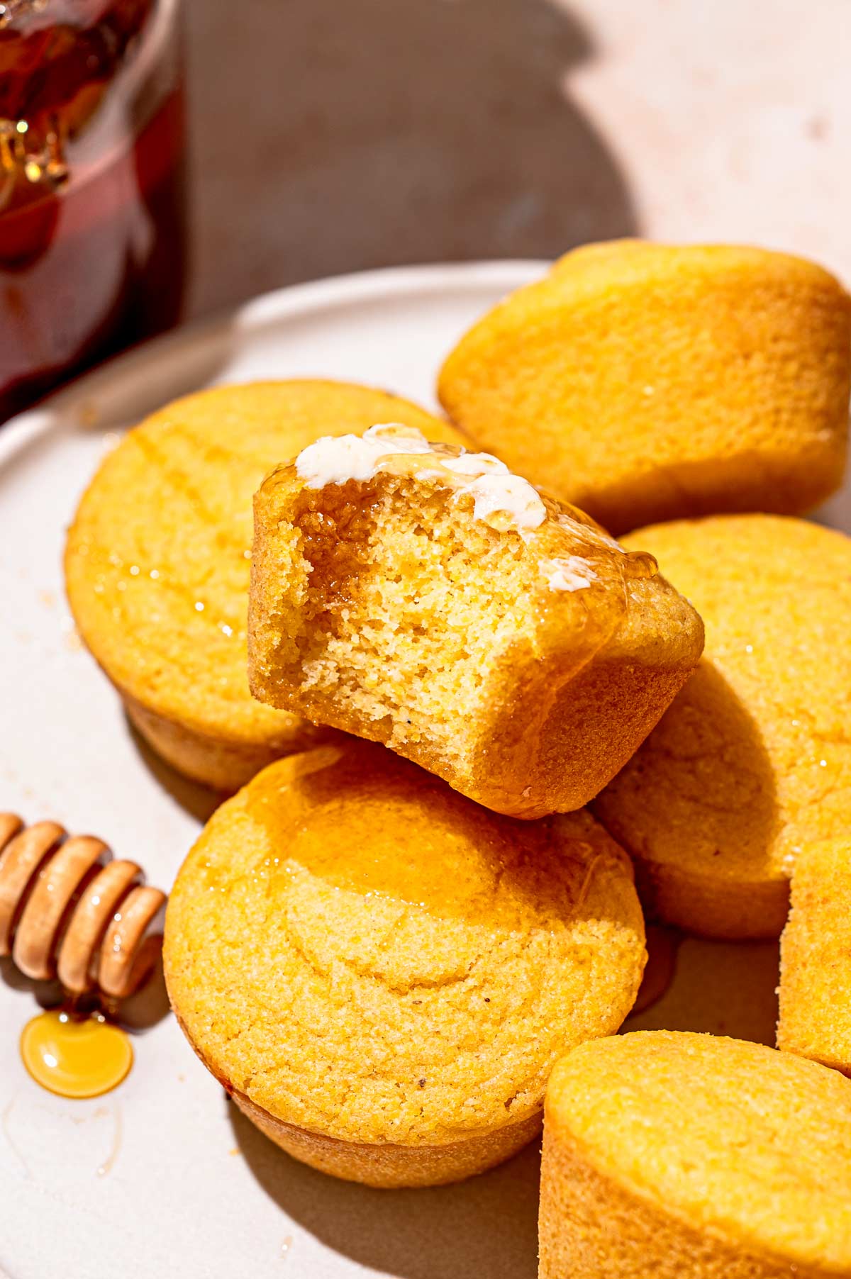 a stack of cornbread muffins without eggs, one of which has a bite taken out exposing the crumb.