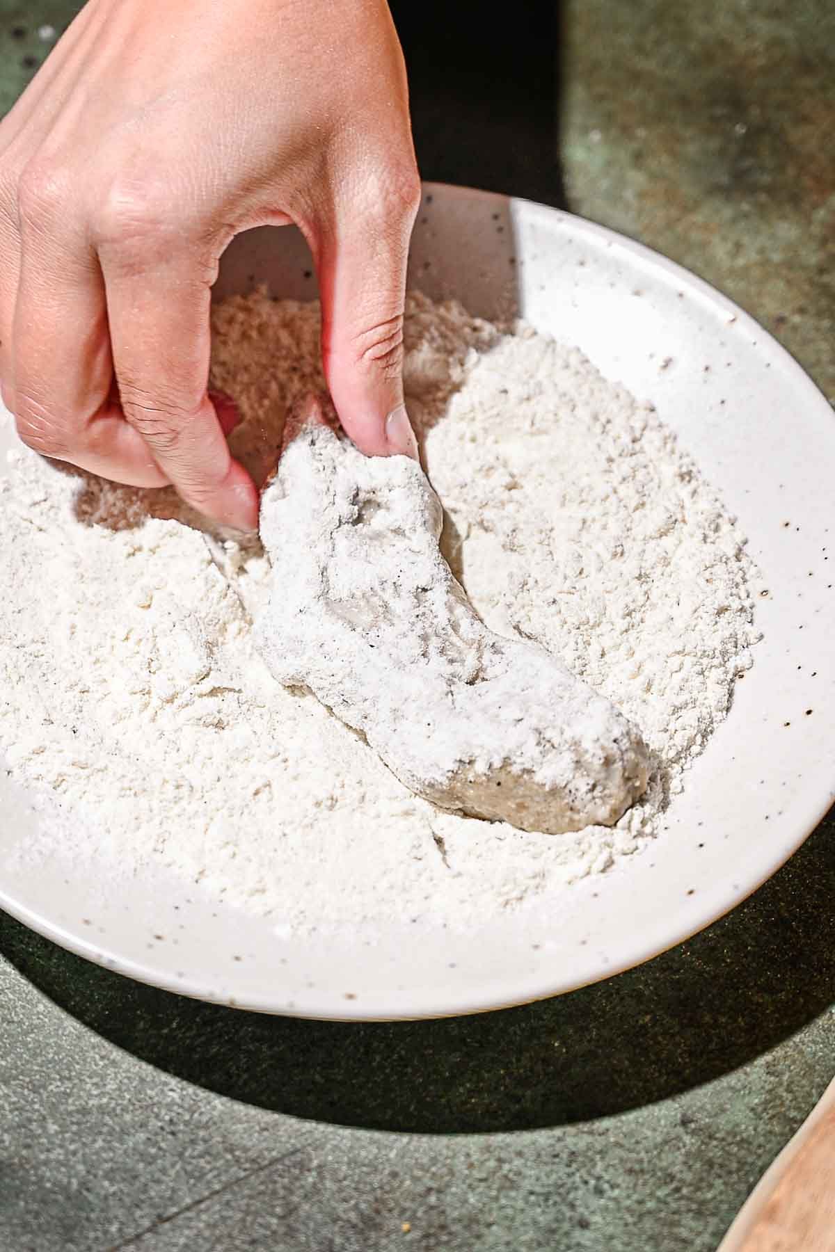 a hand coating the vegan chicken in flour.