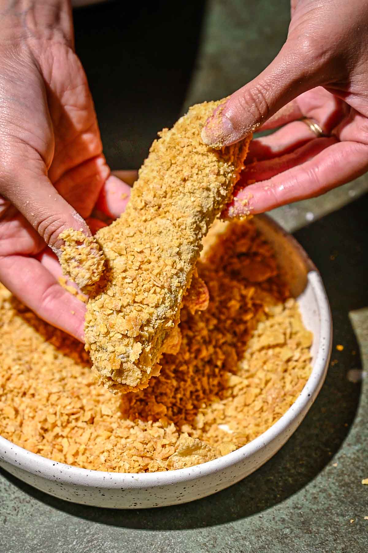 a hand coating the seitan tender in crushed cornflakes.