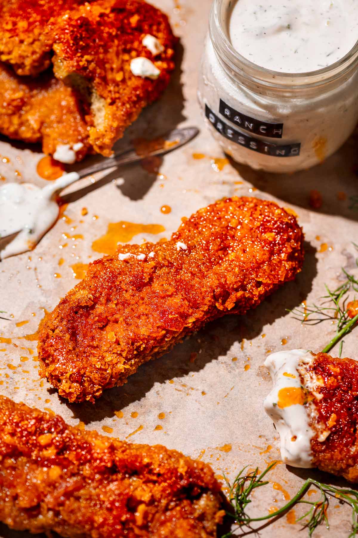 a vegan buffalo chicken wing or tender with a jar of vegan ranch behind it.