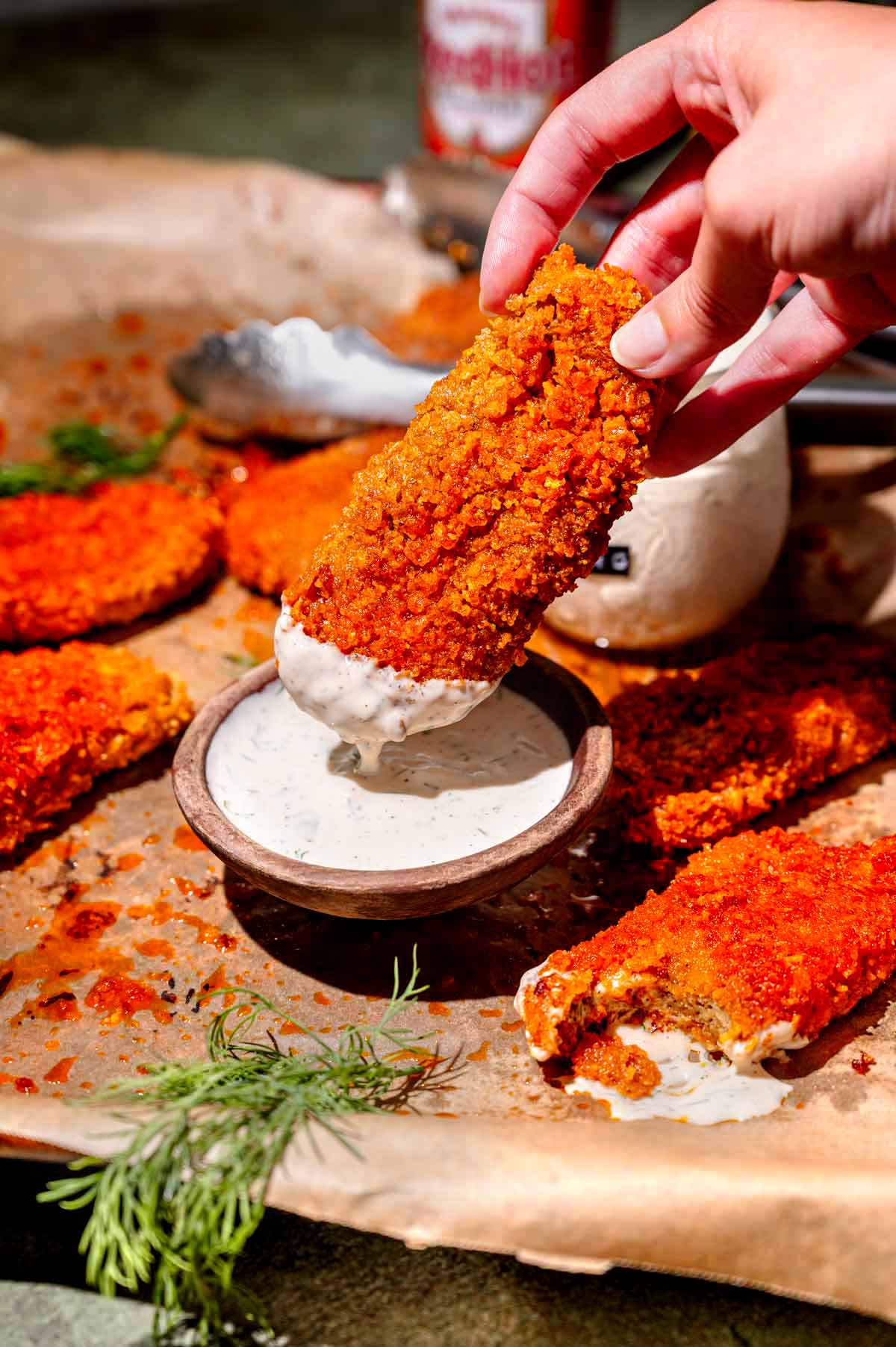 a hand dipping a vegan buffalo chicken wing in ranch.