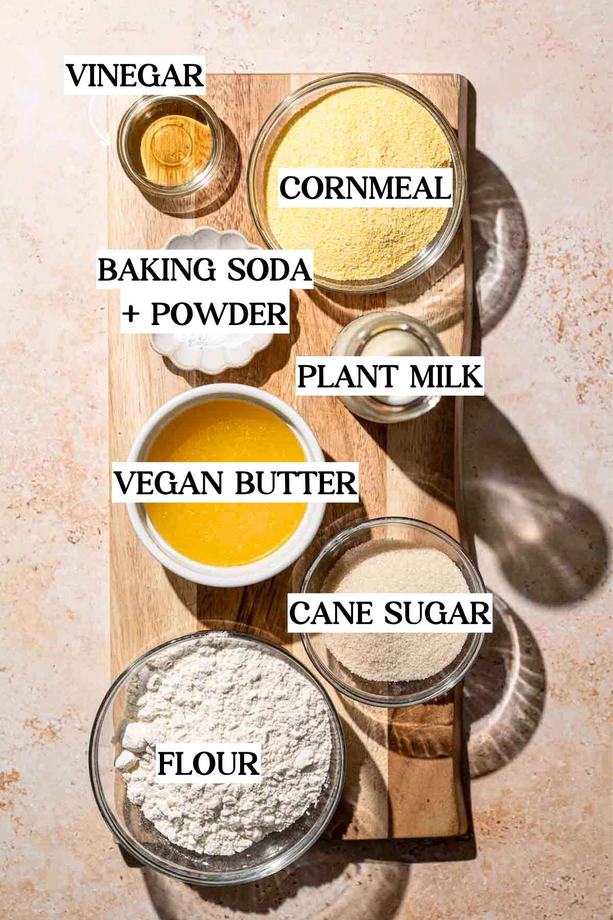 ingredients like cornmeal, flour, baking soda and powder on a wooden cutting board.