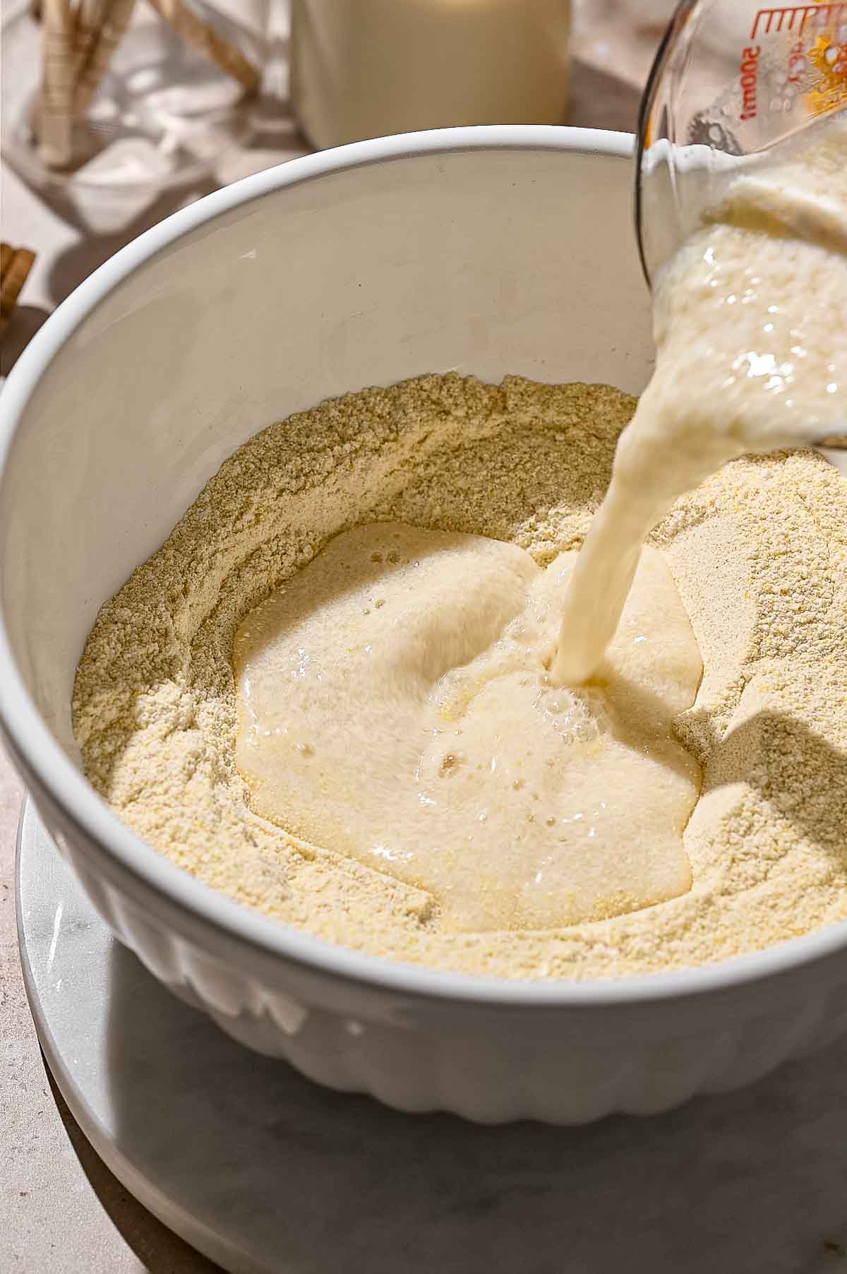 vegan buttermilk being poured into the well in the dry ingredients for the eggless cornbread muffins.