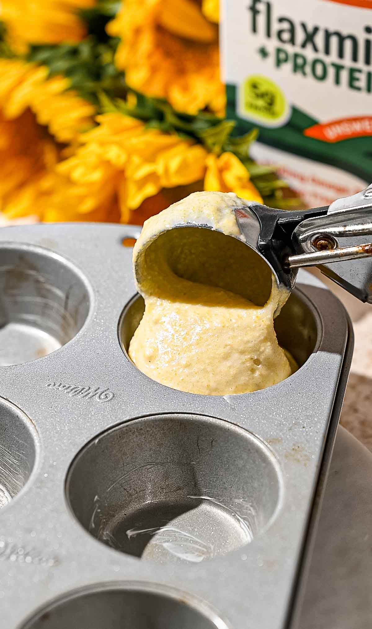 a metal cooking scoop releasing vegan cornbread batter into the muffin tin cup.