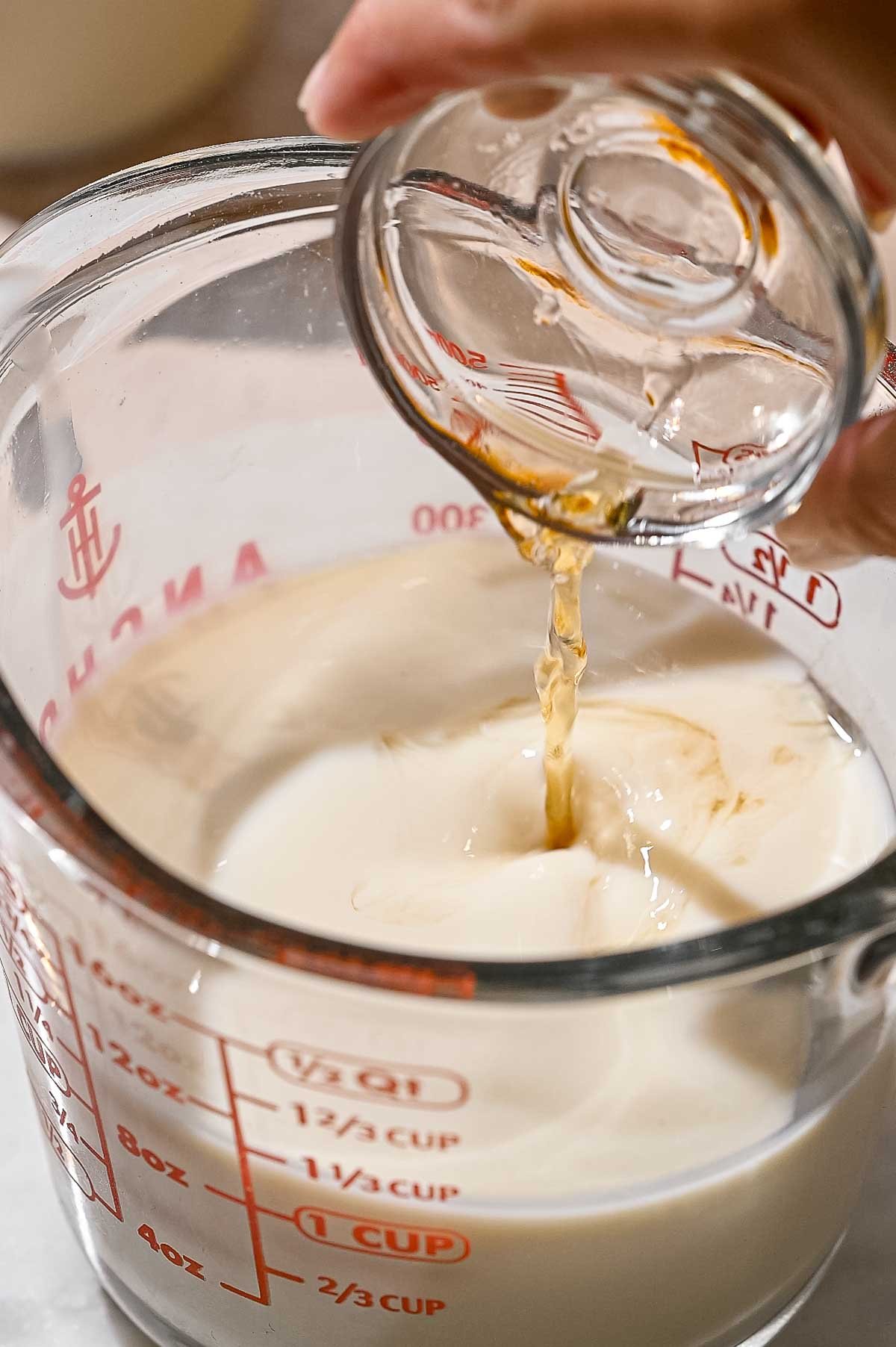 vinegar being poured into a glass measuring cup filled with Flaxmilk.