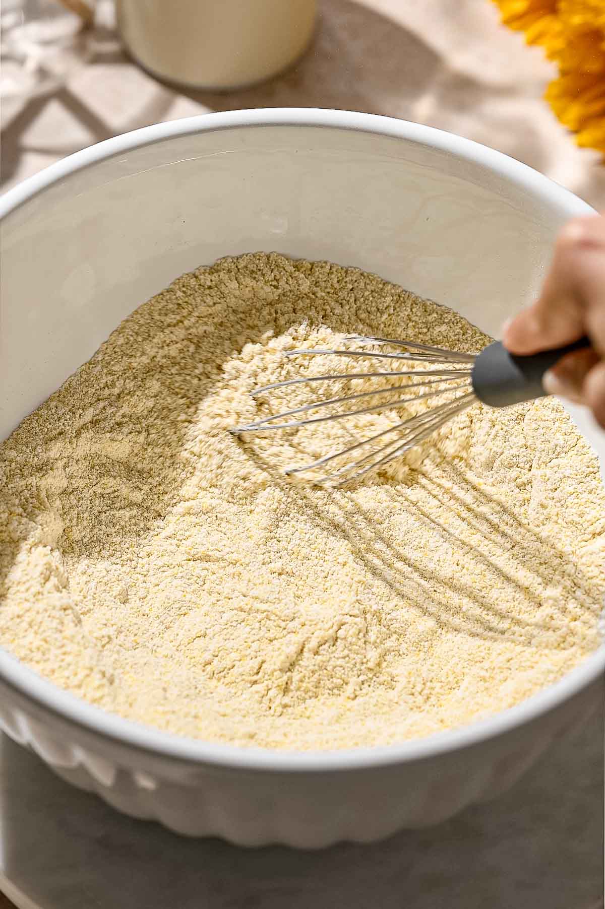 a hand whisking the dry ingredients together in a large bowl.