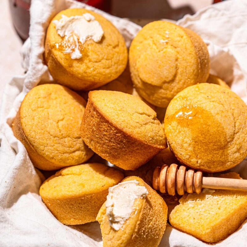 a bowl lined with a linen cloth filled with vegan cornbread muffins.