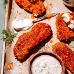 a vegan buffalo chicken tender on a parchment lined baking sheet with ranch dressing.