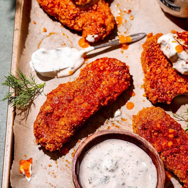 a vegan buffalo chicken tender on a parchment lined baking sheet with ranch dressing.