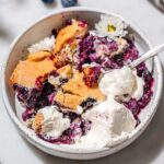vegan blueberry cobbler with whipped cream in a white ceramic dish.