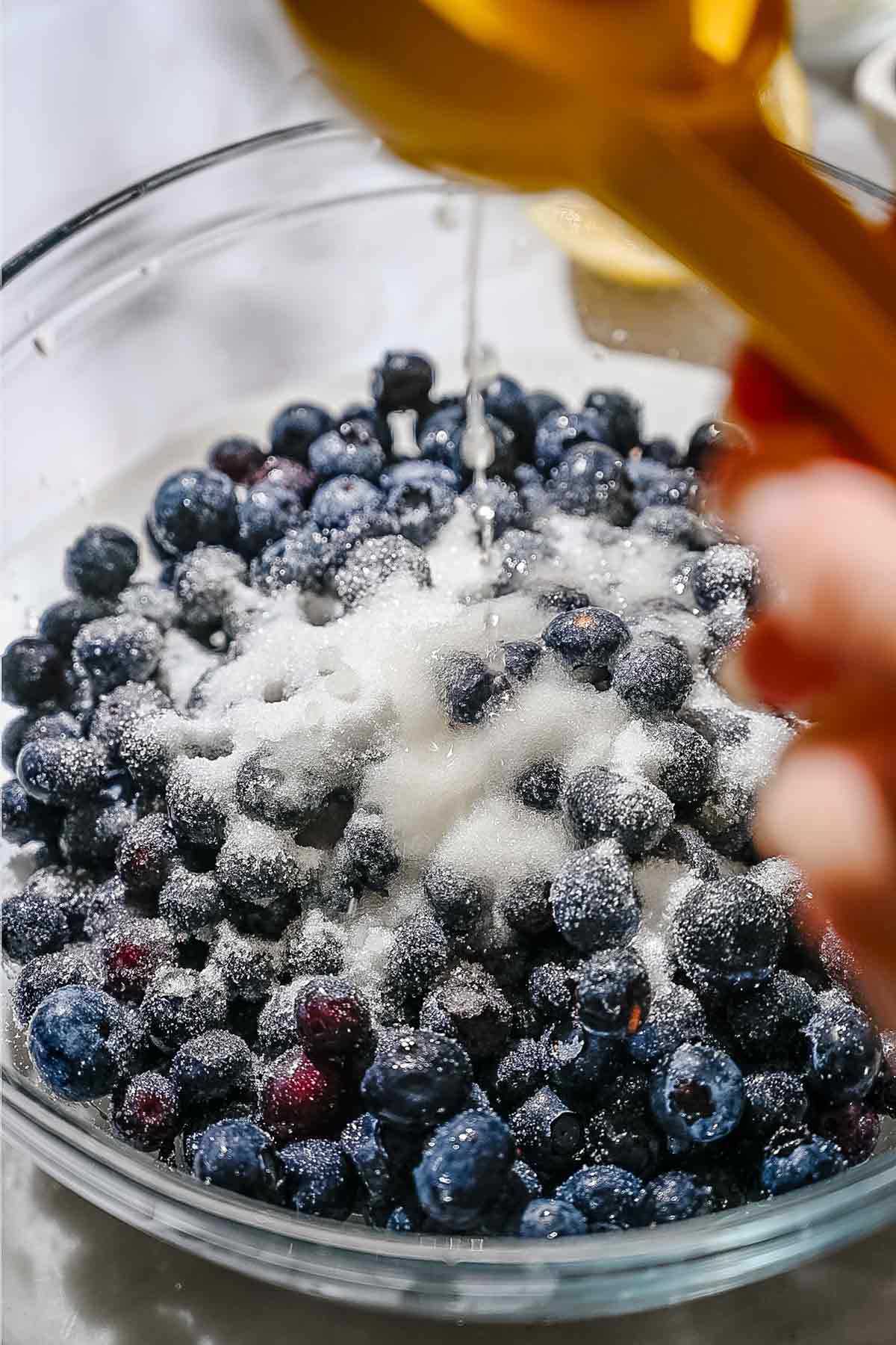 a hand squeezing lemon juice on blueberries and sugar.