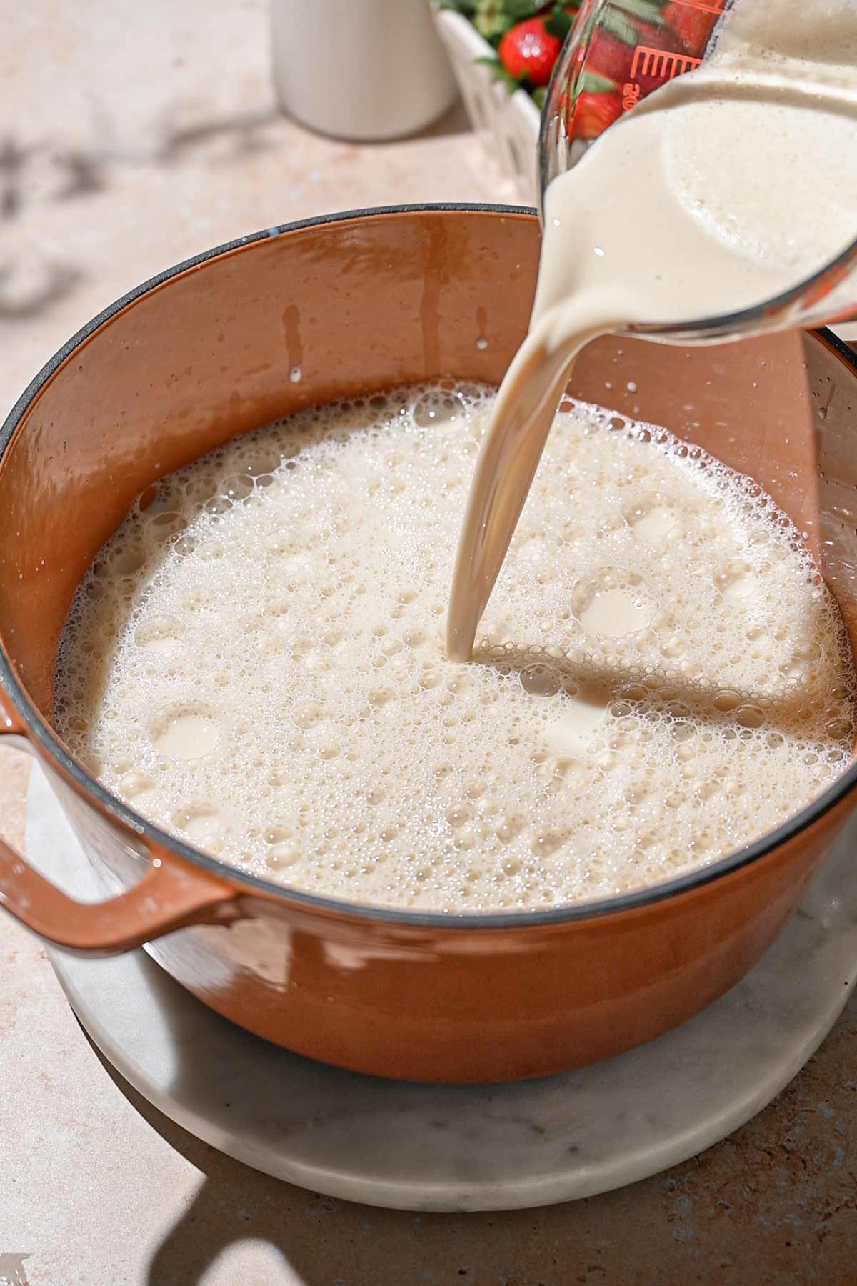 a pitcher of soy milk being poured into a Dutch oven.