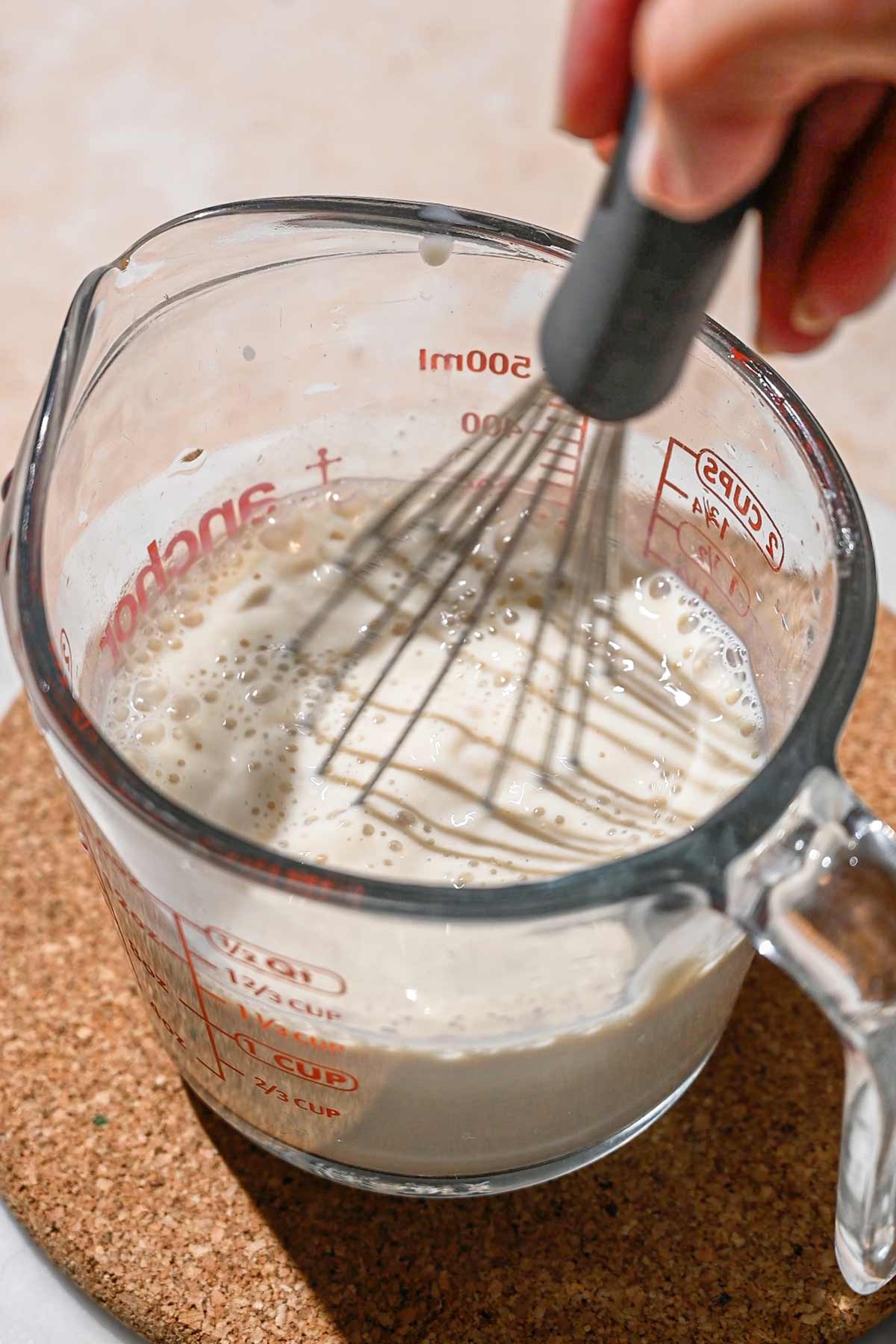 a hand whisking the yogurt starter into the cooled soy milk.
