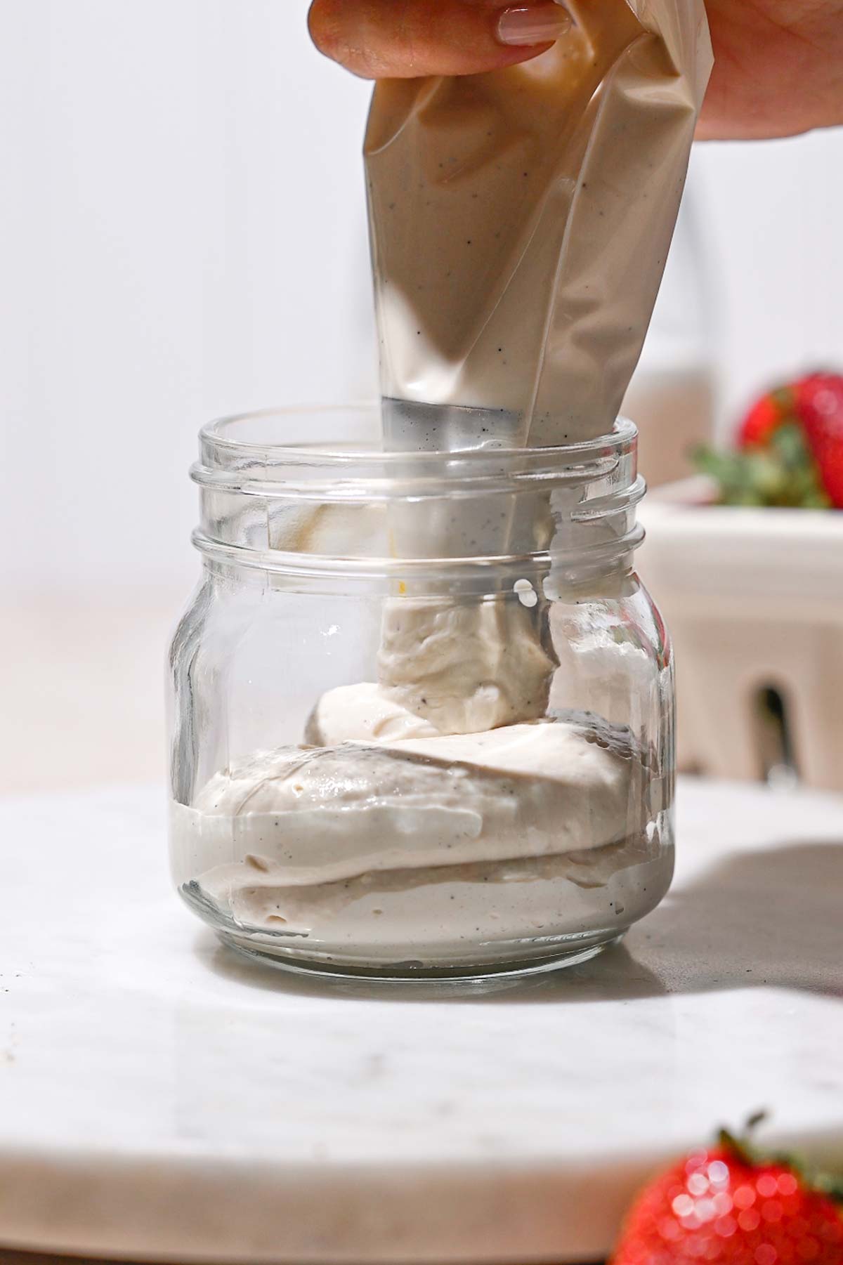 a hand piping the yogurt into a jar.