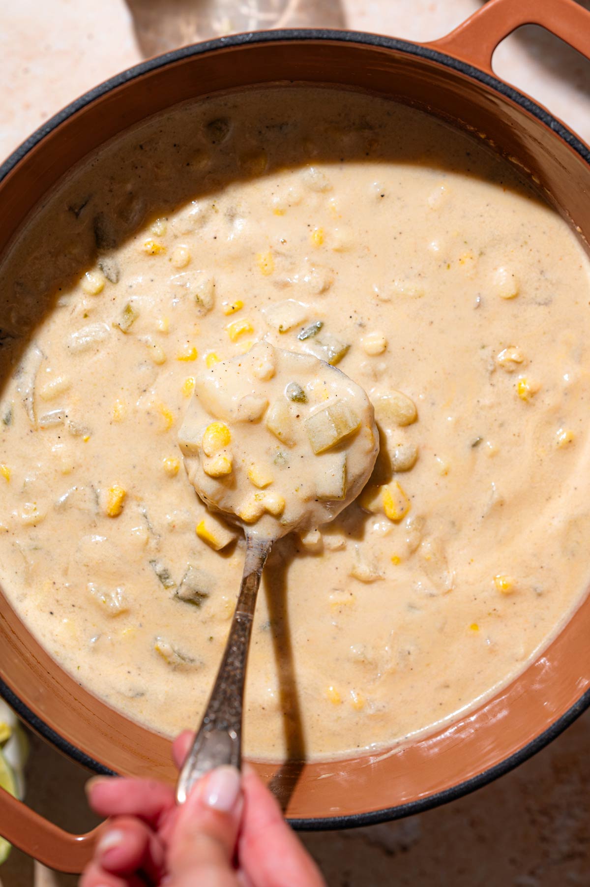 a Dutch oven with vegan corn and potato chowder and a ladle spooning it.