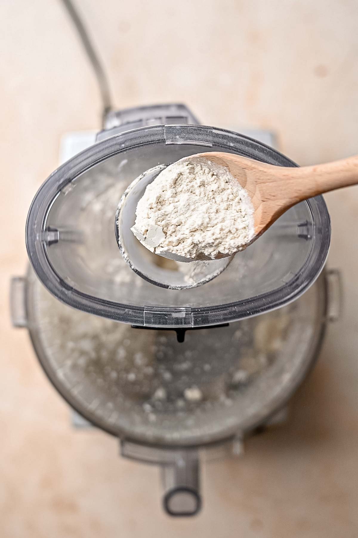 a wooden spoon adding vital wheat gluten to a food processor.