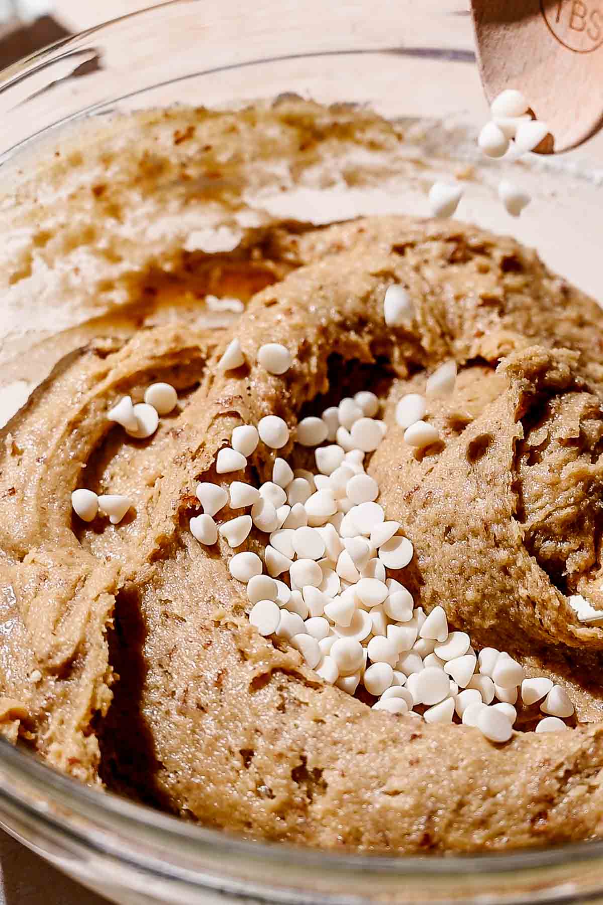 a wooden spoon adding vegan white chocolate chips to the blondie batter.