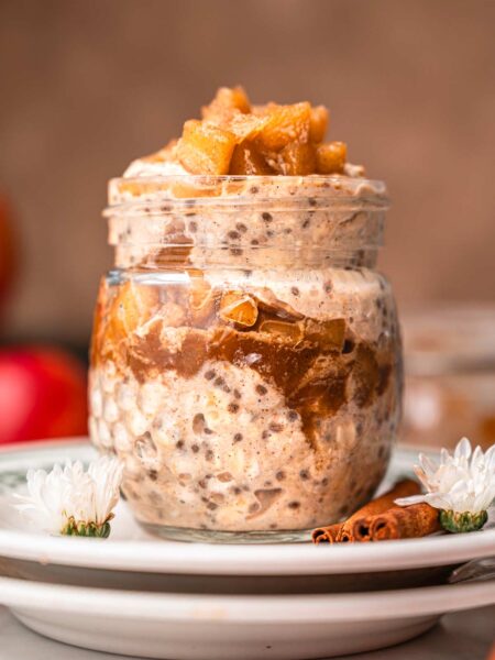 easy apple cinnamon overnight oats in a glass jar on a stack of plates.