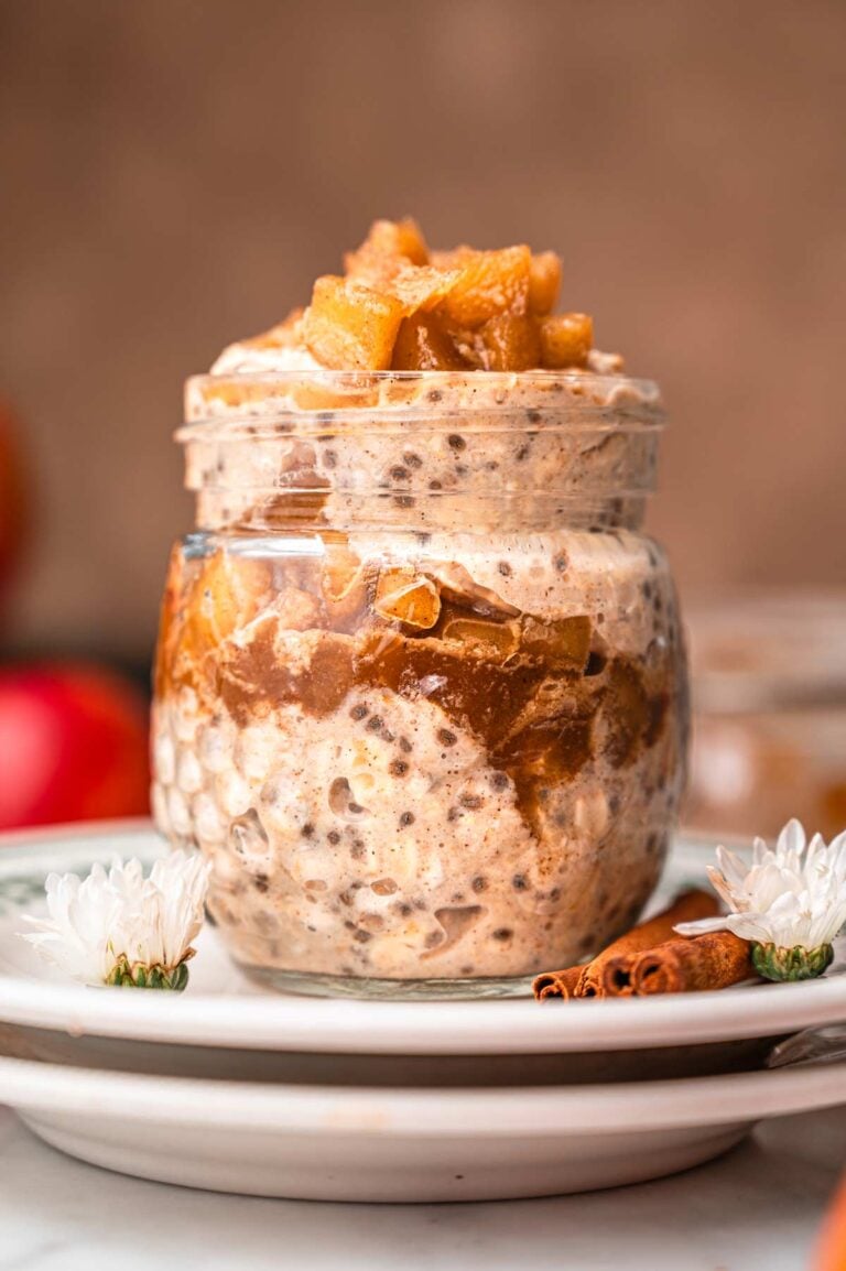 easy apple cinnamon overnight oats in a glass jar on a stack of plates.