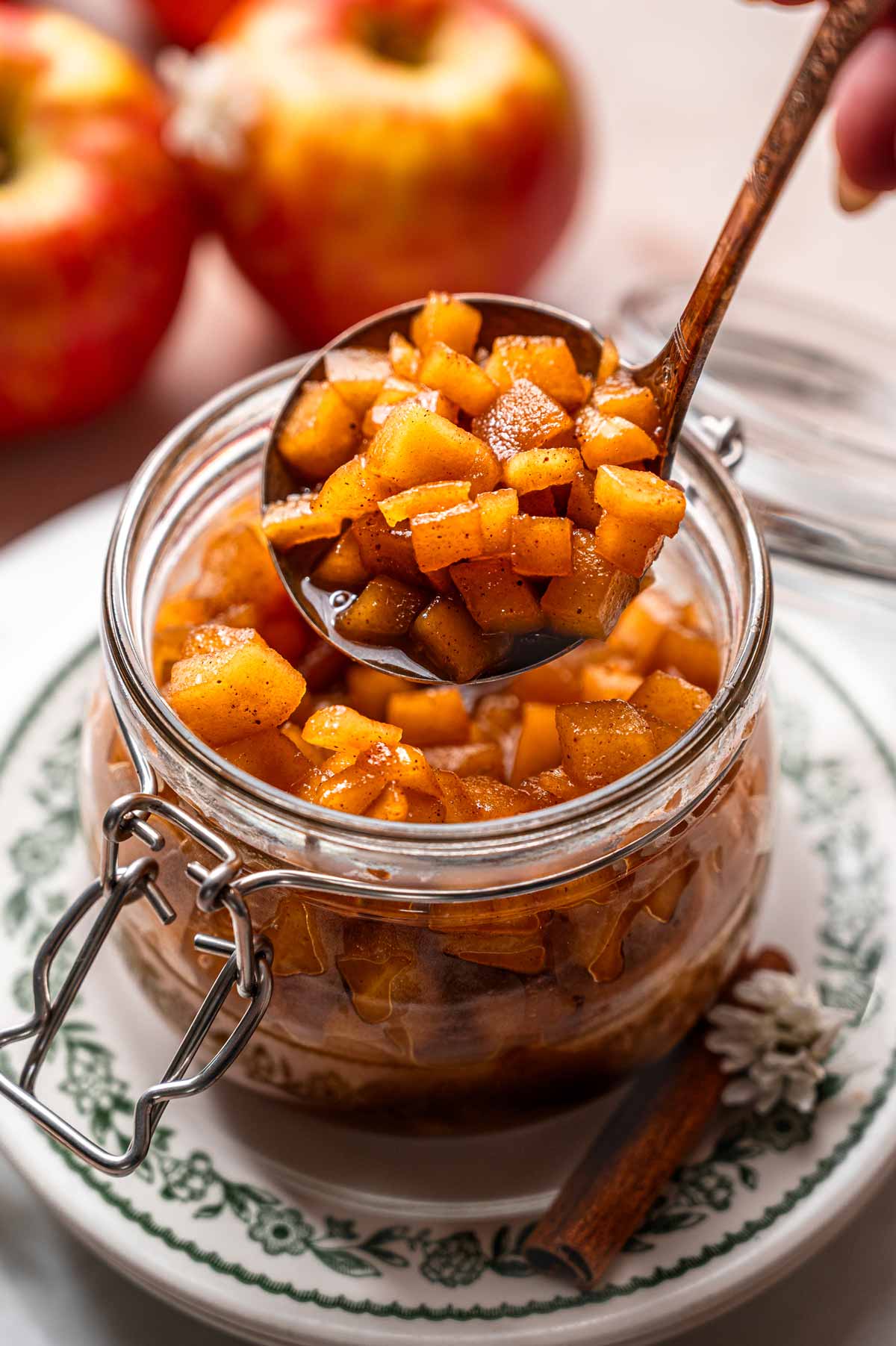 a hand using a ladle to spoon homemade caramelized apples into a glass jar.