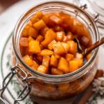 a glass container filled with tender caramelized apples on a stack of vintage green plates.