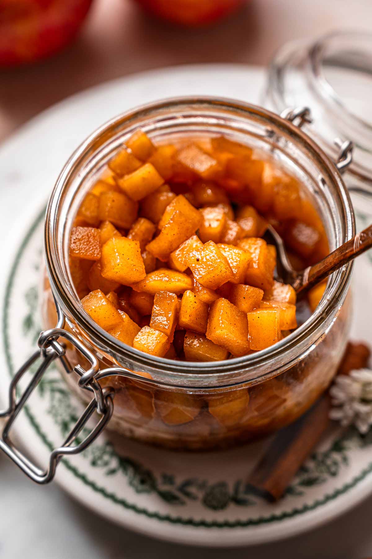 a glass container filled with tender caramelized apples on a stack of vintage green plates.