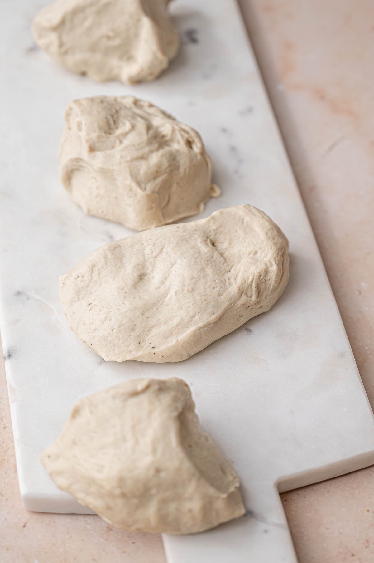 seitan dough divided into four pieces on a marble cutting board.
