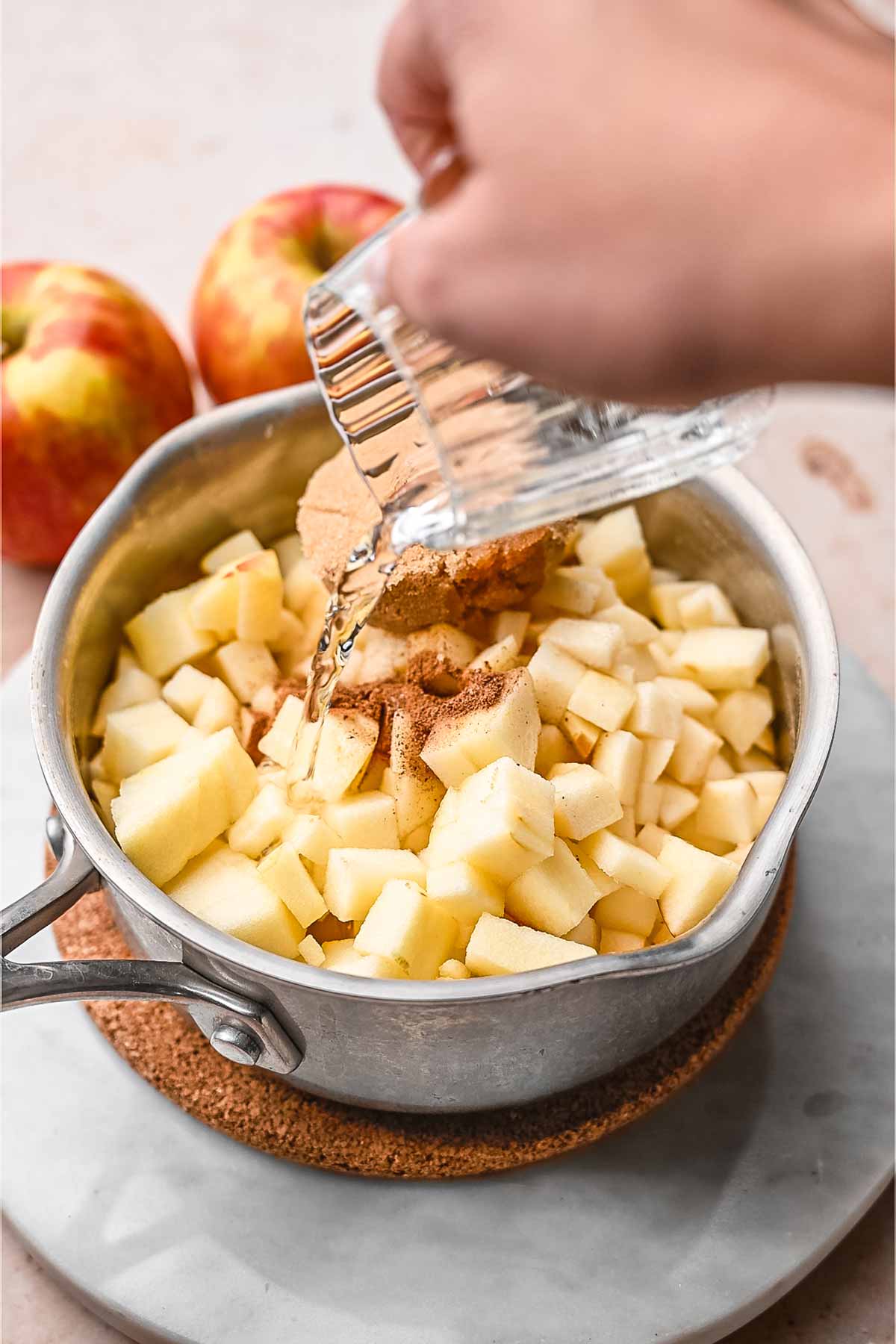 a small stainless steel pot with diced apples, cinnamon and hand pouring water on top.