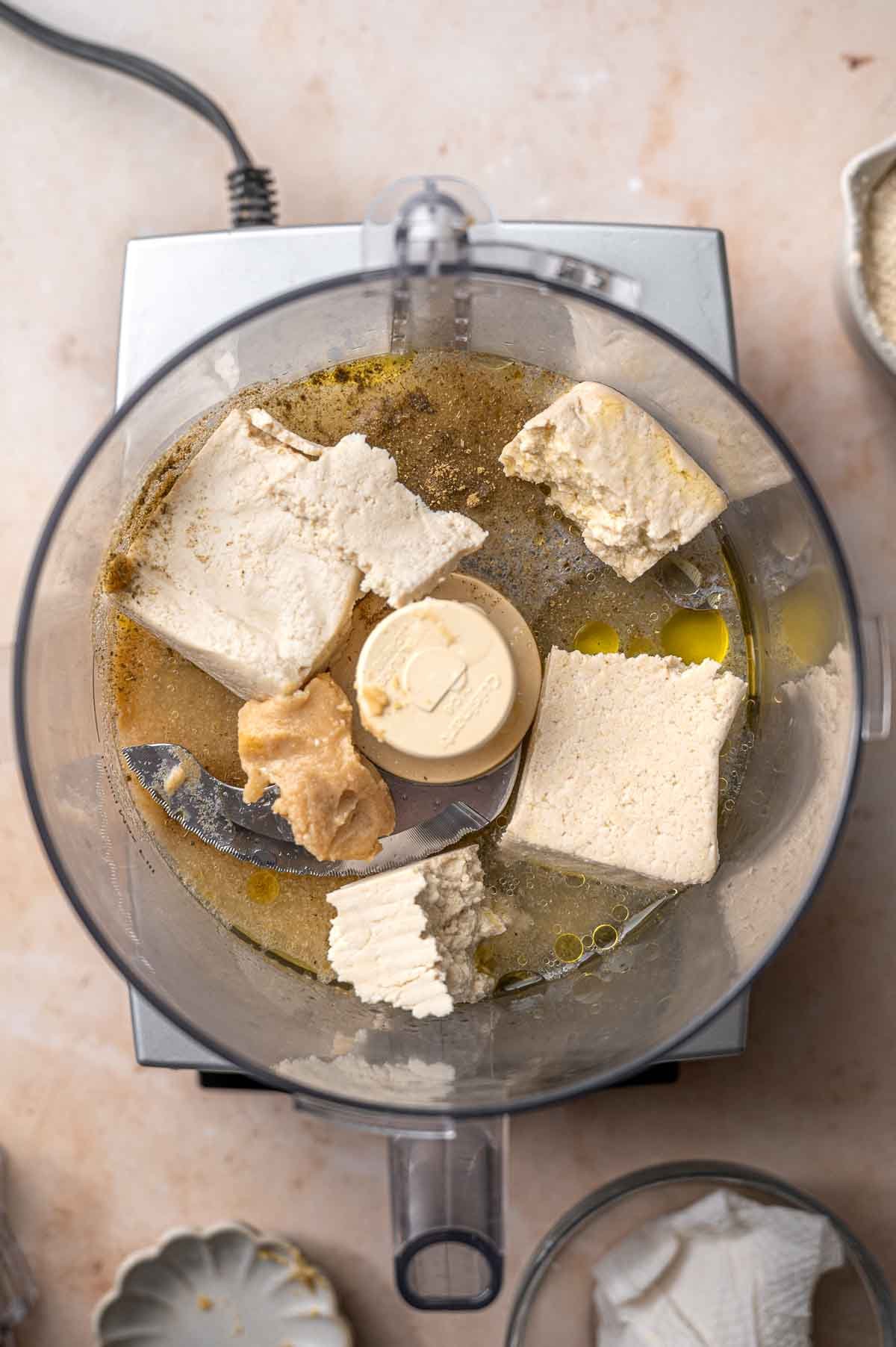 super firm tofu, oil and miso paste in a food processor bowl.