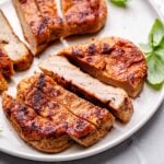 baked vegan chicken breasts sliced on a ceramic plate with a few basil leaves.