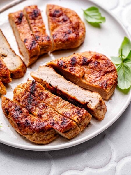 baked vegan chicken breasts sliced on a ceramic plate with a few basil leaves.