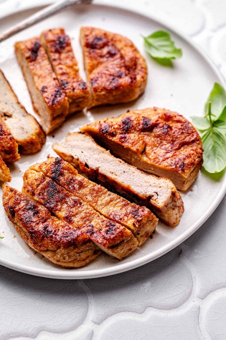 baked vegan chicken breasts sliced on a ceramic plate with a few basil leaves.