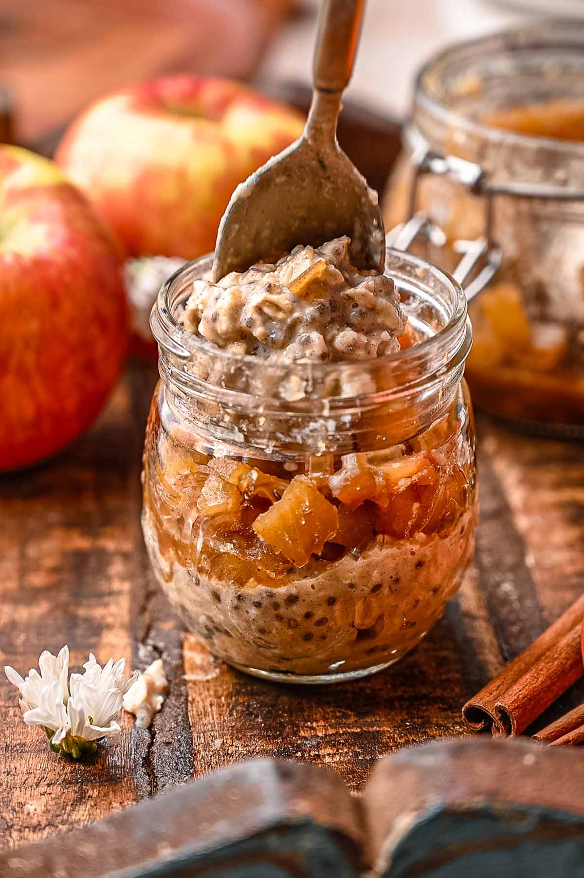 a spoon layering thickened apple cinnamon overnight oats in a glass jar with stovetop apples.