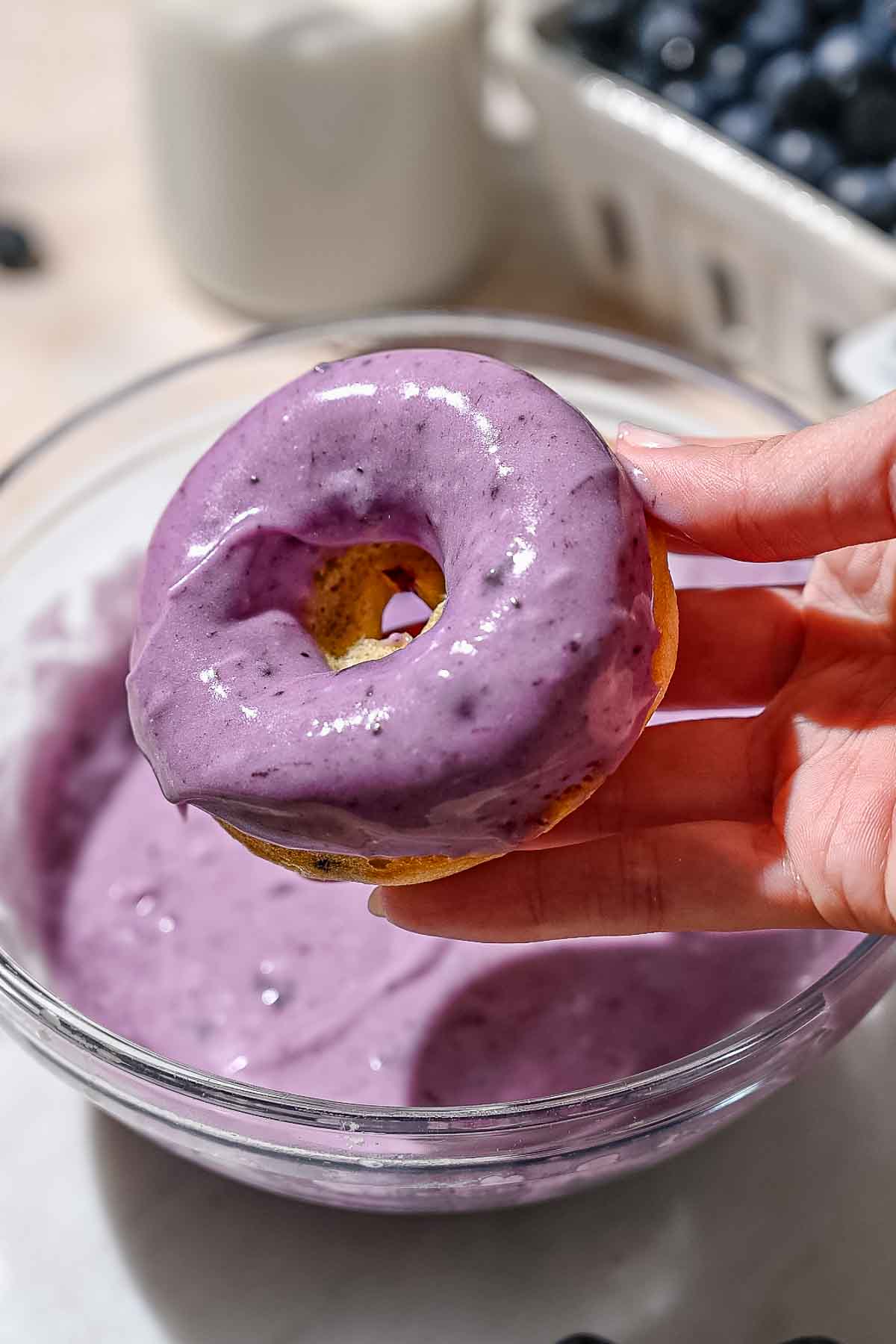 a hand holding a baked blueberry cake donut topped with a blueberry glaze.