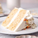 a slice of vegan vanilla cake with buttercream frosting on a plate.