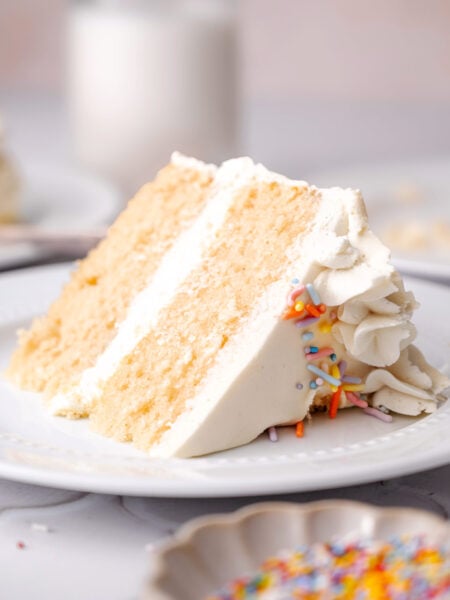 a slice of vegan vanilla cake with buttercream frosting on a plate.