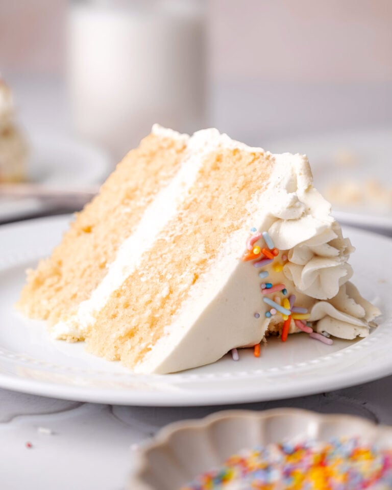 a slice of vegan vanilla cake with buttercream frosting on a plate.