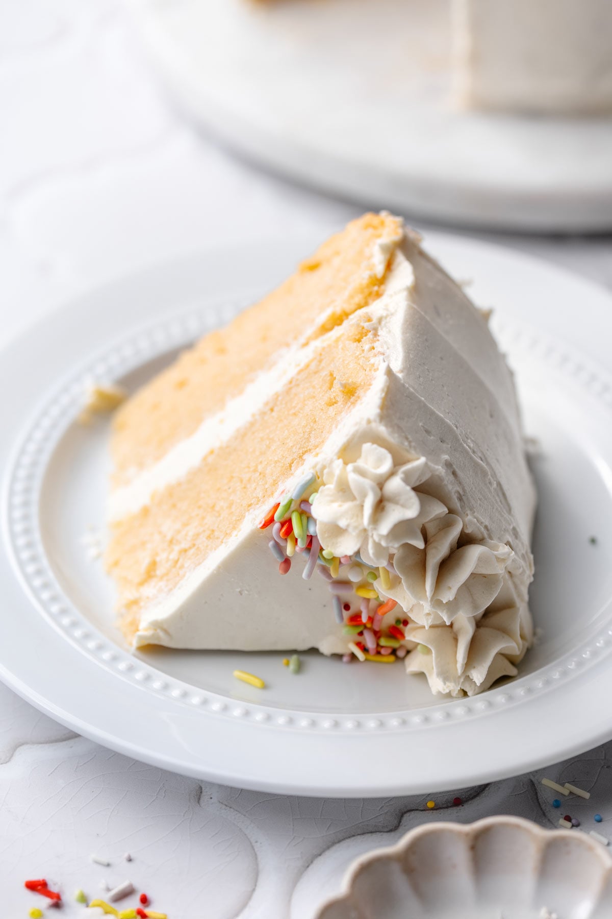 a slice of vegan vanilla cake with buttercream frosting on a plate.